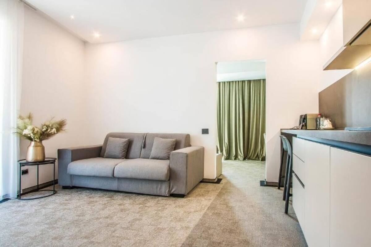 A modern living room with a grey sofa, a small side table with a vase, and a kitchen area with a countertop and cabinets.