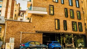 A multi-story building with a brick facade, several windows, and a parking area with cars. - Central Carol ApartHotel 1 (Bucharest)