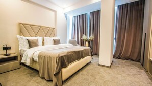 A hotel room with a large bed, a bedside table, a nightstand, and a vase with flowers. - Central Carol ApartHotel 1 (Bucharest)