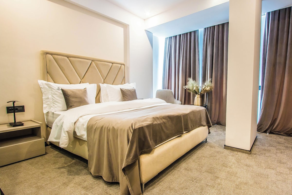 A hotel room with a large bed, a bedside table, a nightstand, and a vase with flowers.