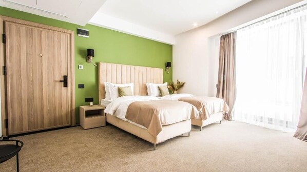 Ett hotellrum med två sängar, en garderob, sängbord och ett stort fönster med gardiner.