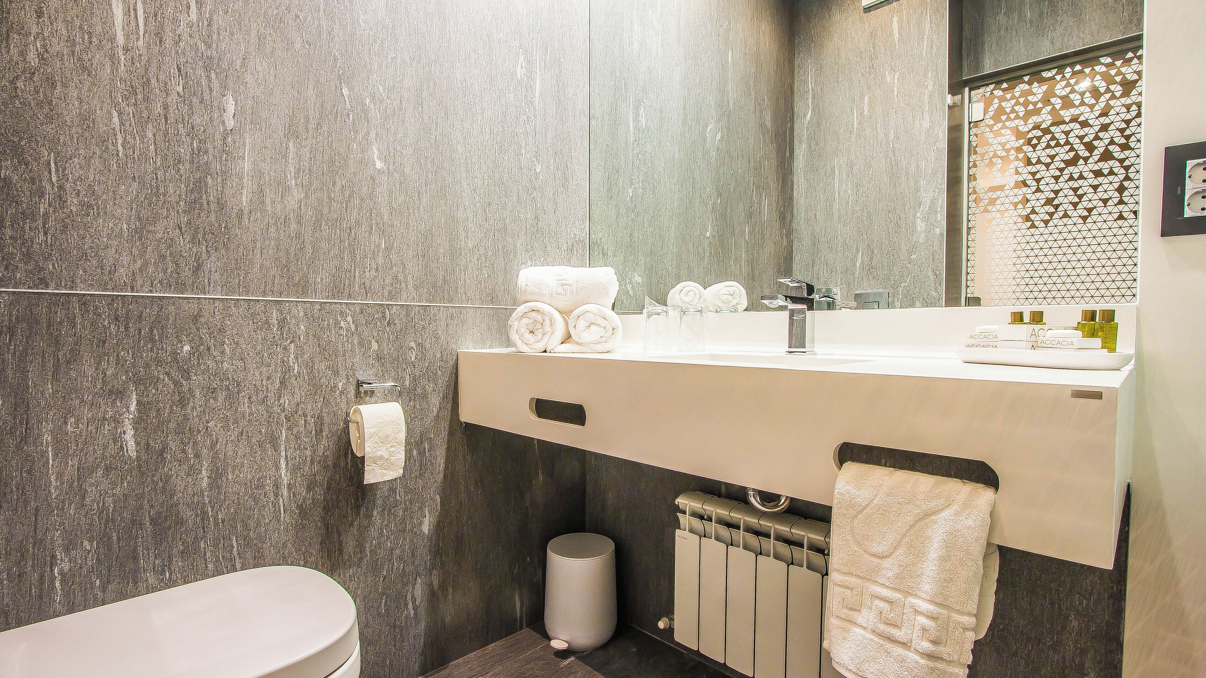 A modern bathroom with a marble wall, a sink with toiletries, and a toilet.