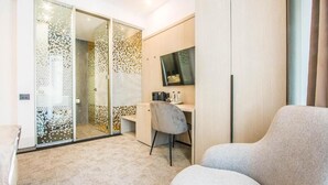 A modern hotel room with a sliding glass door leading to a balcony, a desk with a chair, and a flat-screen TV mounted on the wall. - Central Carol ApartHotel 1 (Bucharest)