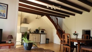 A cozy living area with a wooden dining table, a kitchen in the background, and a staircase leading upstairs. - Maison de Campagne au Calme, for lovers of nature and beautiful walks (La Chapelle-de-Brain)