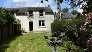 A two-story house with a fenced backyard, a patio table with chairs, and a garden with pink flowers. - Maison de Campagne au Calme, for lovers of nature and beautiful walks (La Chapelle-de-Brain)