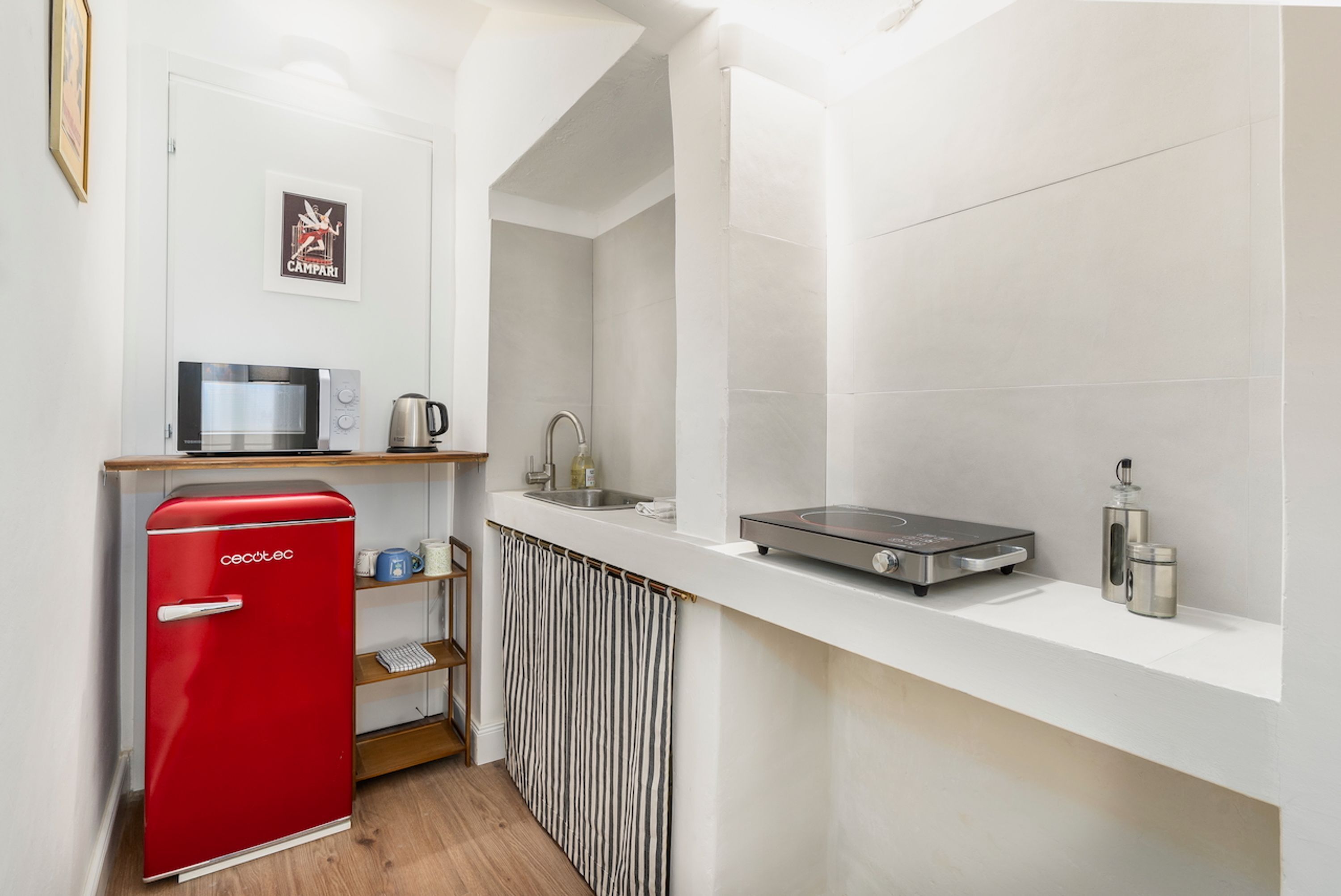 A compact kitchen with a red refrigerator, a microwave, a kettle, and a coffee maker on the counter.
