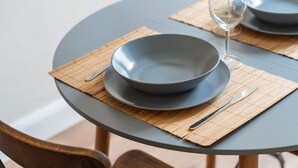 Ein runder Esstisch mit dunkelblauer Tischdecke, einem dunkelblauen Teller, einem Weinglas und einem Holzstuhl mit Metallbeinen.