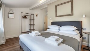 Ein ordentlich bezogenes Bett mit weißen Leinen und Handtüchern, ein Holzboden, ein Kleiderständer und ein gerahmtes Bild an der Wand.