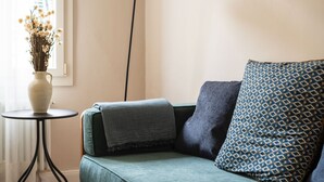 Ein gemütliches Zimmer mit einem türkisfarbenen Sofa, einem gemusterten Kissen, einer Vase mit getrockneten Blumen und einem kleinen runden Tisch.