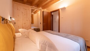 Un dormitorio con techo de madera, una cama con ropa de cama blanca, un armario de madera y una puerta que da a otra habitación.