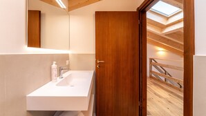 Un baño moderno con puerta de madera, lavamanos blanco y tragaluz.