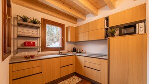 Una cocina moderna con armarios de madera, microondas integrado y ventana con vista a árboles.