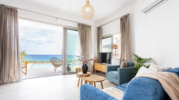 A modern living room with a sofa, a TV, and a view of the ocean.