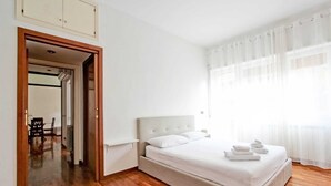 A bedroom with a bed, wooden flooring, a door leading to a hallway, and a window with sheer curtains. - Quiet and charming house near Trastevere (Roma)