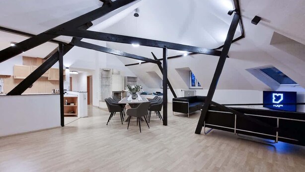 A spacious loft-style room with a high ceiling, exposed beams, a dining area with a table and chairs, and a modern kitchen in the background. - Alpha Apartments: Grand Loft for 8, Roof Terrace (Krefeld)