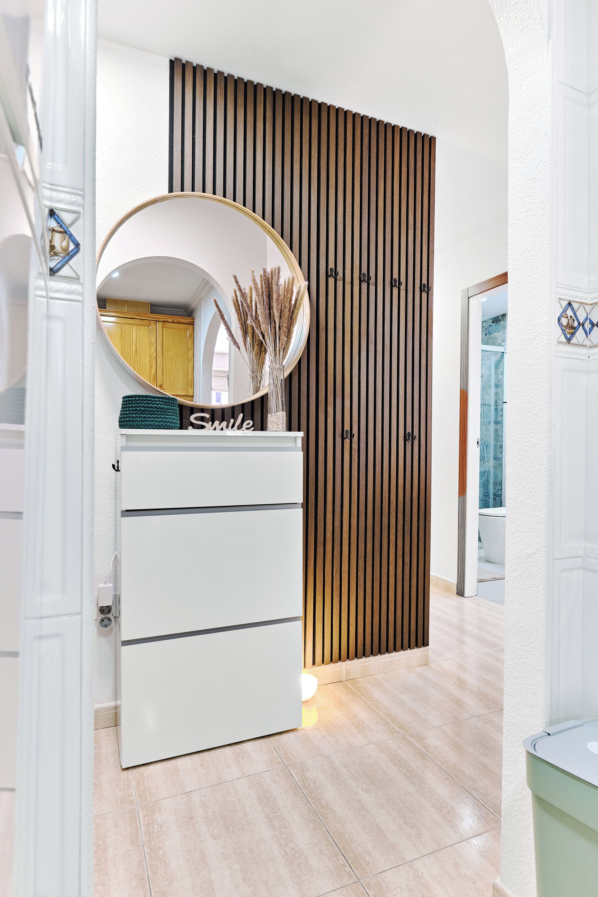 Une salle de bain moderne avec un meuble-lavabo blanc, un miroir rond et un mur recouvert de panneaux en bois.