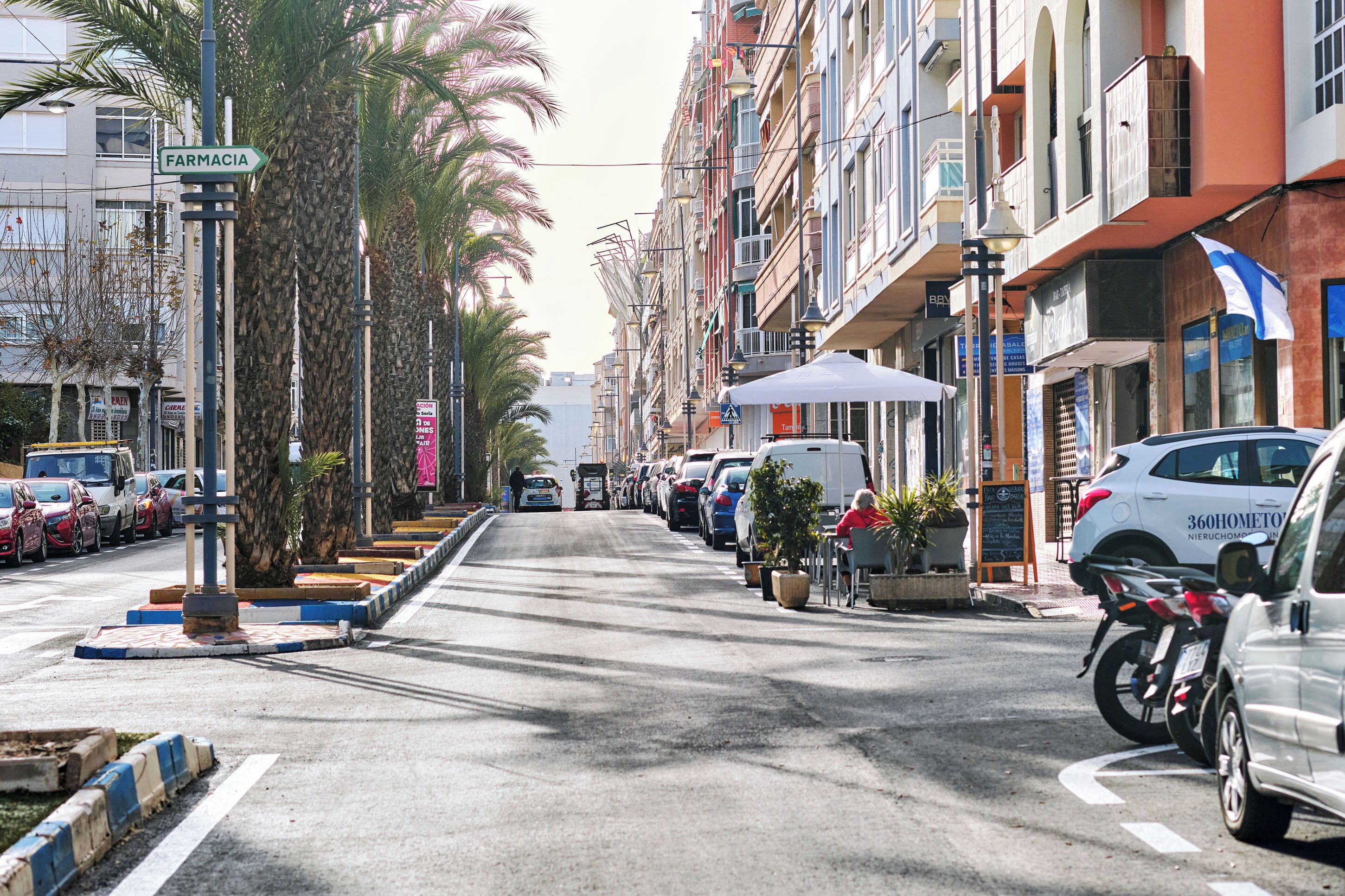 Une rue bordée de voitures garées, une pharmacie reconnaissable à son enseigne, et des immeubles dotés de balcons.