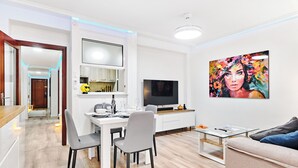 A modern living room with a dining area, a flat-screen TV, and a large painting on the wall.