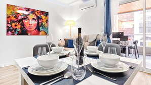 A dining area with a table set for two, a painting on the wall, and a view of the outside.