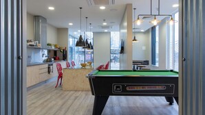 A modern indoor space with a pool table, a kitchen area, and a seating area with red chairs.