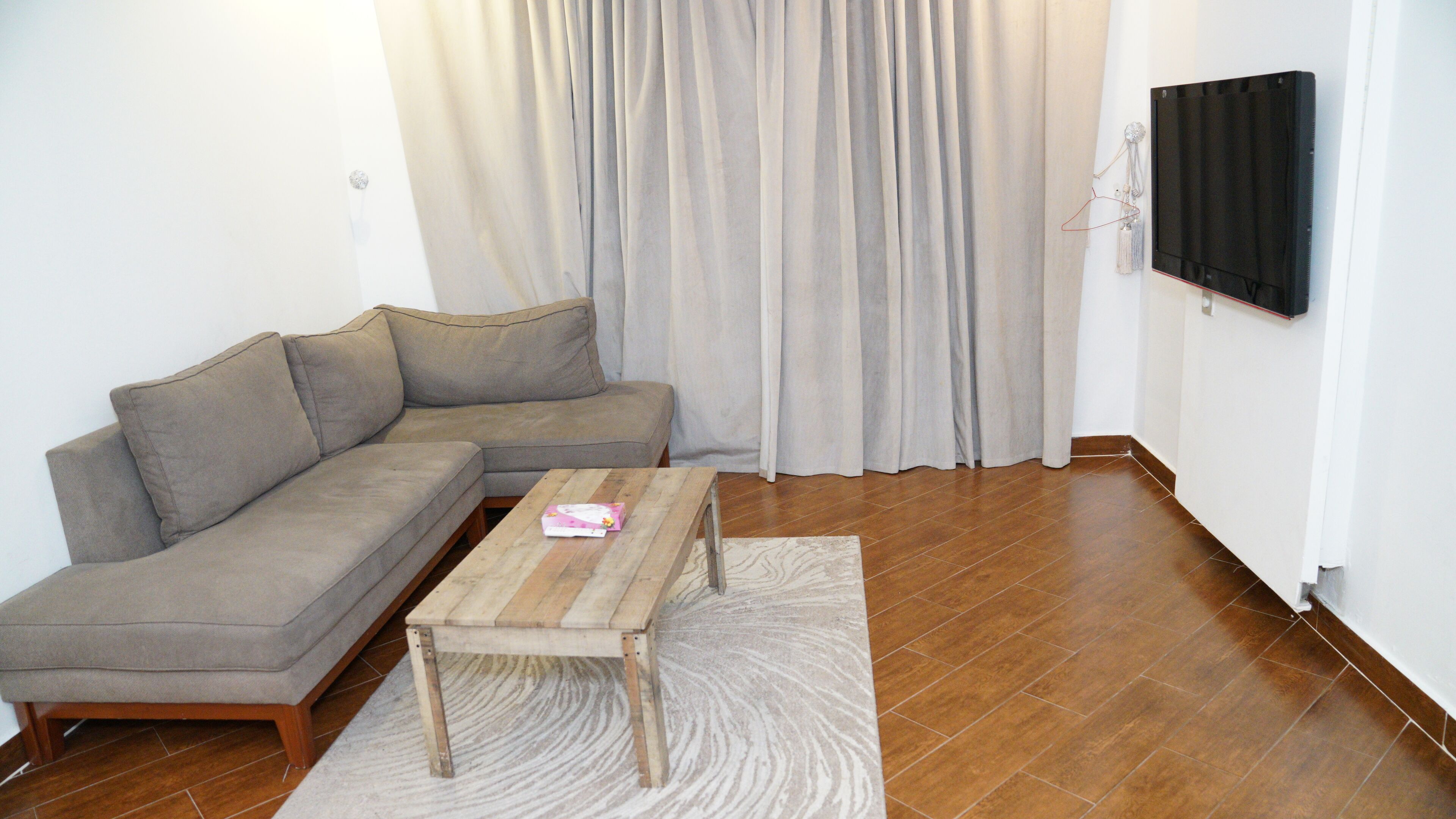 A living room with a grey sectional sofa, a wooden coffee table, a patterned rug, and a black TV on the wall.
