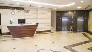 A hotel reception area with a wooden reception desk, a clock, and an elevator.