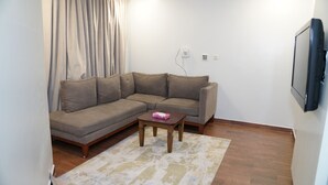 A living room with a brown sectional sofa, a small wooden coffee table, and a TV mounted on the wall.