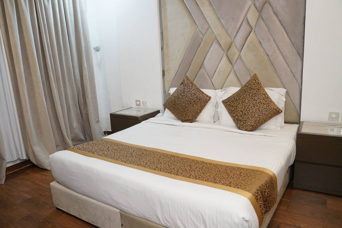 Une chambre d’hôtel avec un grand lit, une tête de lit ornée d’un motif géométrique, deux tables de chevet et un plancher en bois.