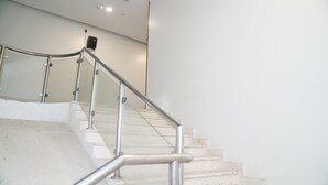 A staircase with a metal handrail and glass panels, leading to a landing with a light switch and a power outlet.