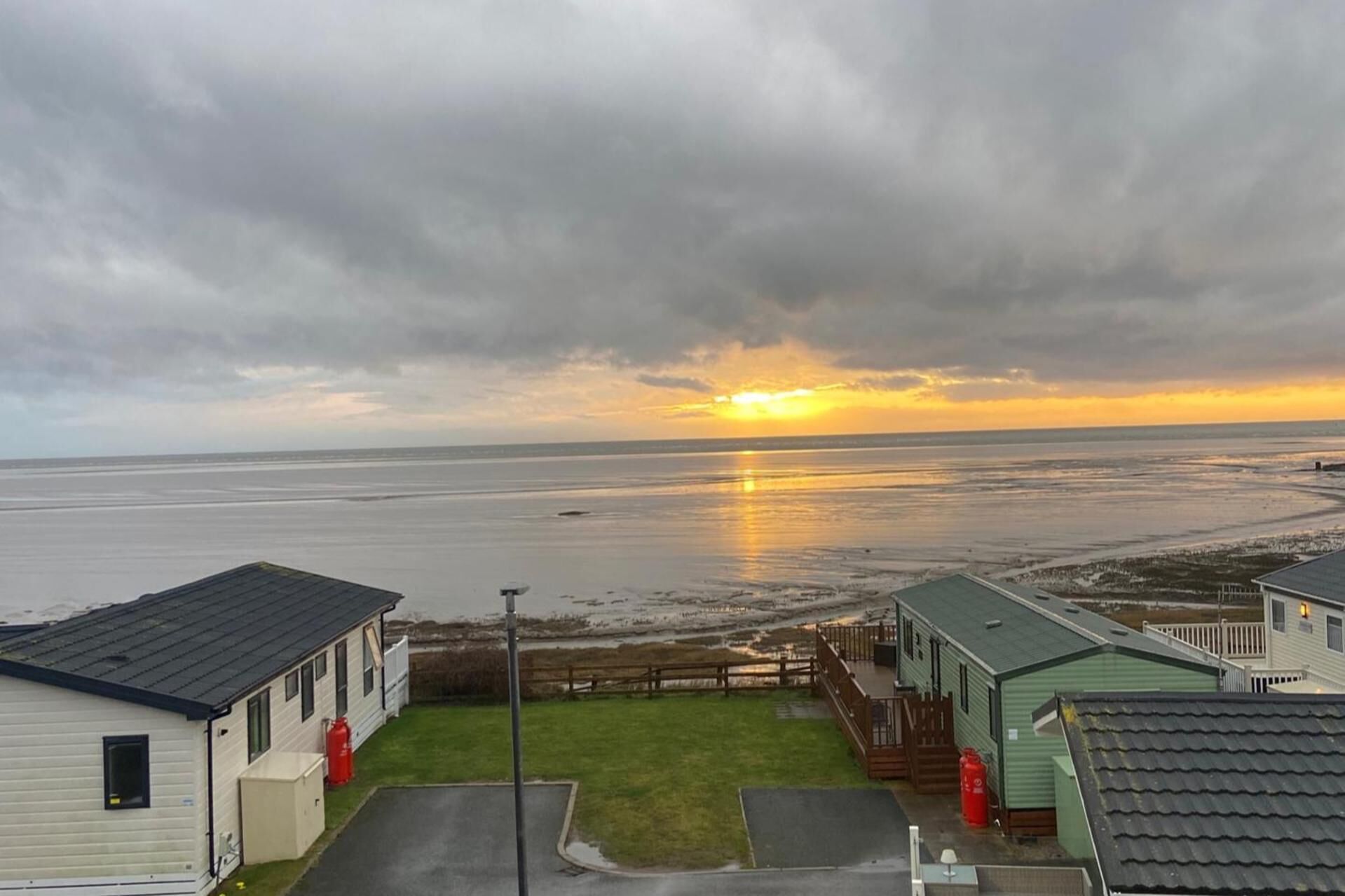 A view of a beach with a sunset, a small parking area, and two mobile homes.