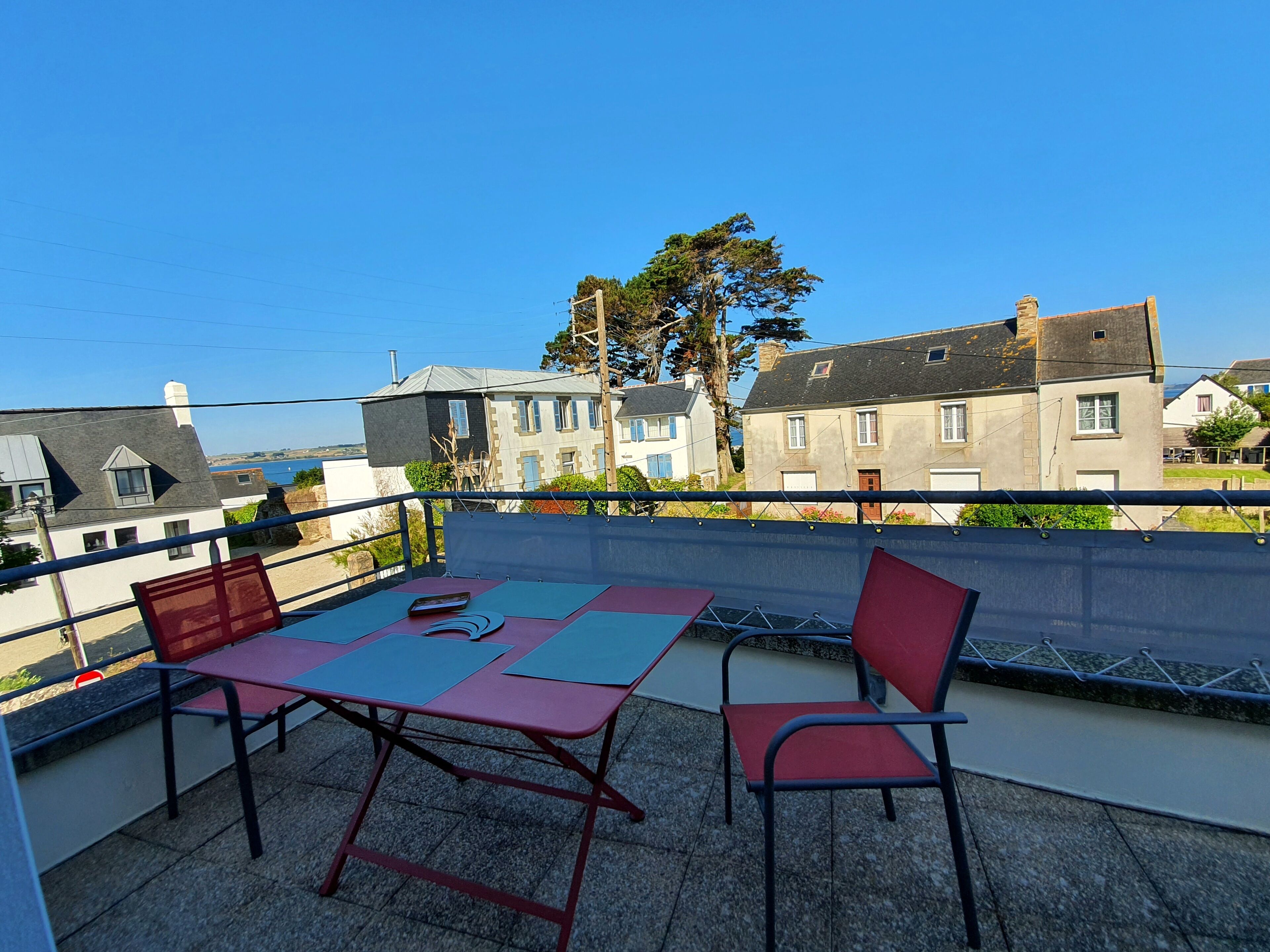 Un balcón con mesa y sillas, con vista a una zona residencial con casas y un cielo despejado.