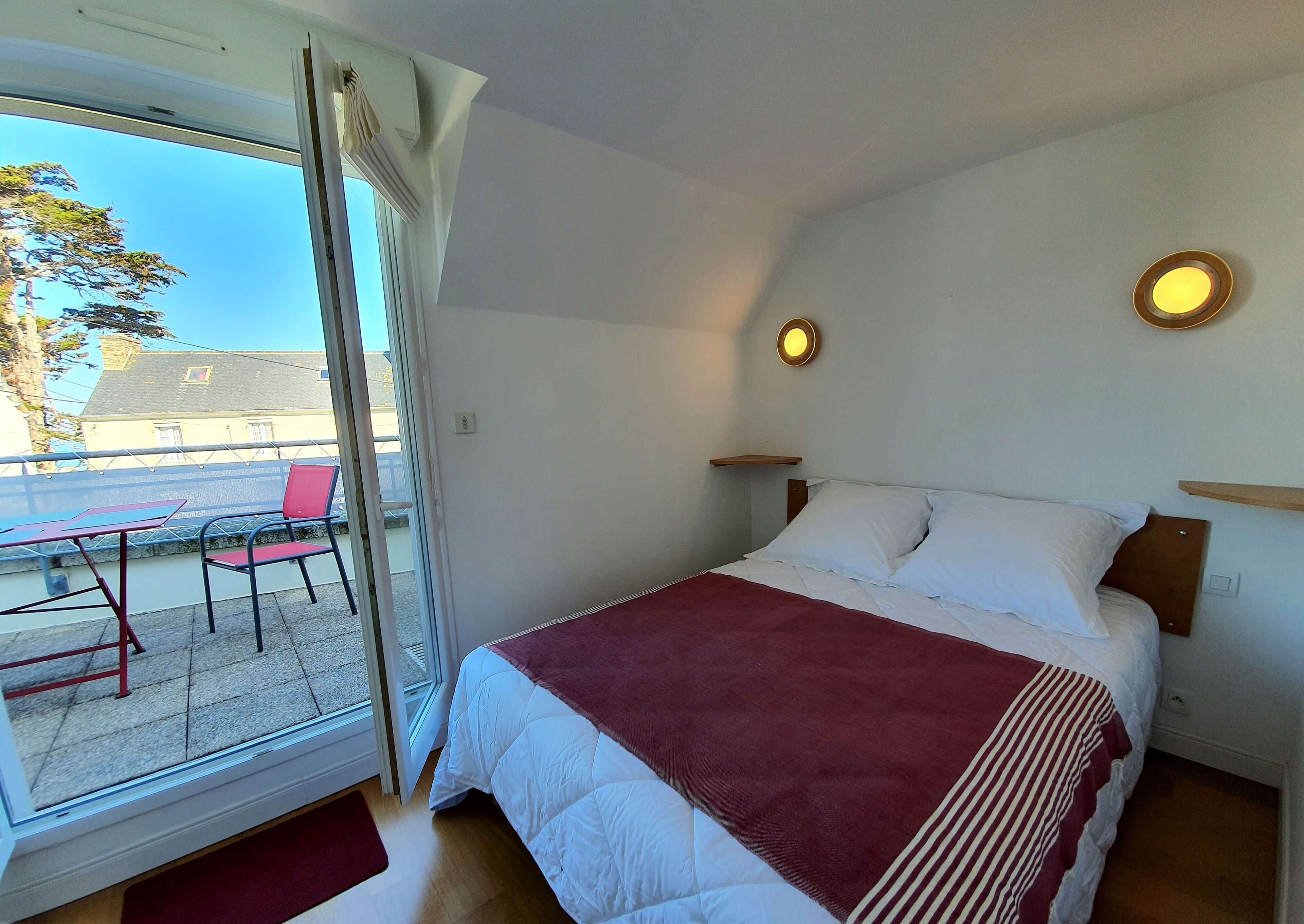 A bedroom with a bed, a window, and a view of the outside.