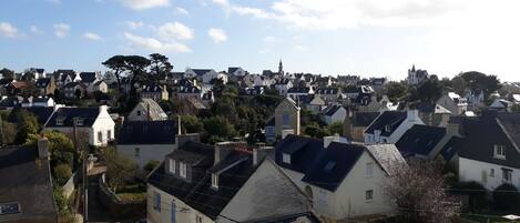 A residential area with houses, some with sloped roofs and others with flat roofs. There are trees and a clear sky.
