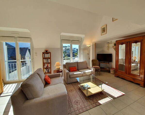 A spacious living room with a sofa, armchair, and a coffee table. There is a bookshelf, a television, and a large mirror. - Duplex Villa Porspol - Terrace with sea view (Carantec)
