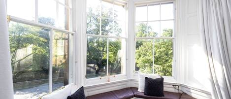 A bay window with a built-in bench, white walls, and a view of trees and a fence.