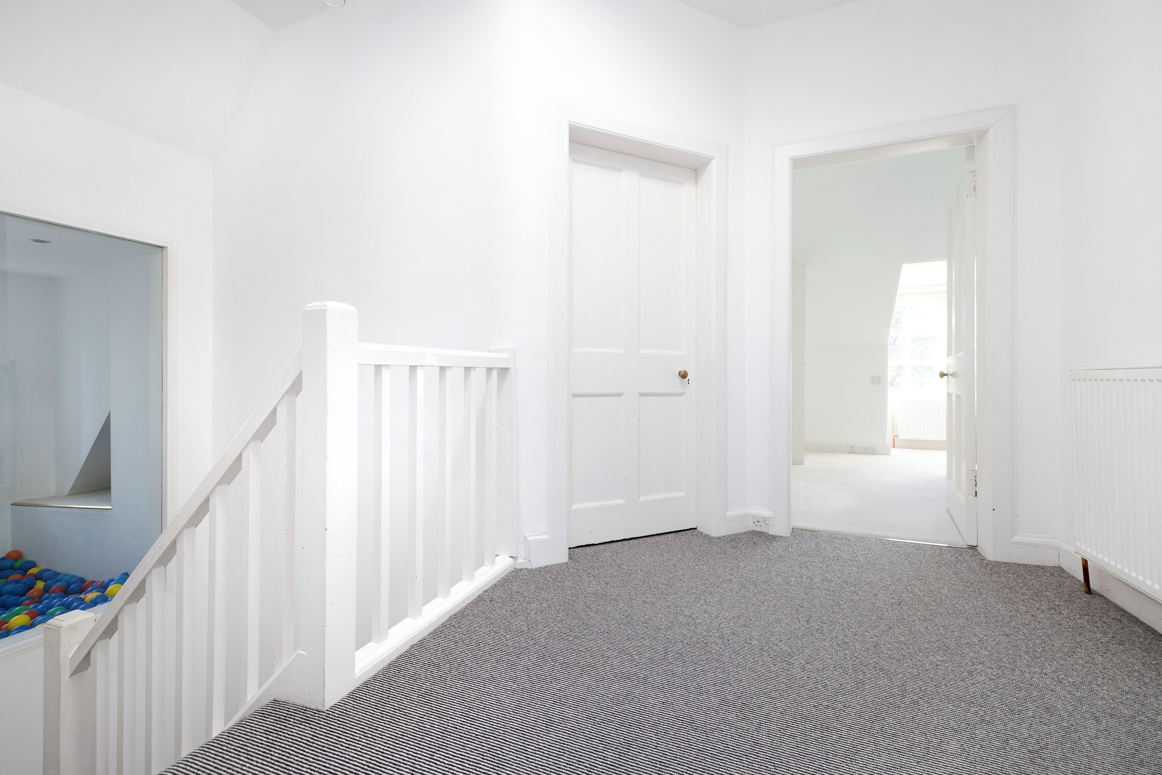 A hallway with white walls, a grey carpet, and a white door.