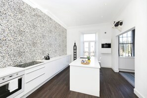 A modern kitchen with a central island, dark wooden flooring, and a wall covered in a cityscape print. - Delightful 3-bed Flat with Parking  (Edinburgh)