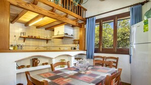 Una cocina con vigas de madera, salpicadero de azulejos, una mesa con colcha y un refrigerador.