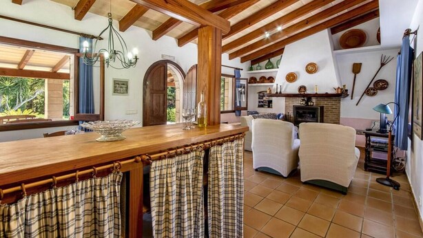 Una cocina rústica con vigas de madera, una zona de bar y un área de estar con sillas.