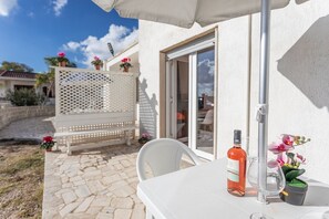 Eine Terrasse mit einem weißen Tisch, einer Weinflasche und einem Glas. Auf dem Tisch steht ein weißer Stuhl und ein kleiner Blumentopf.