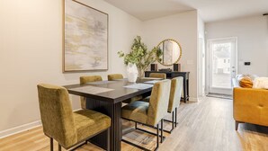 A dining area with a long table, six chairs, a vase with plants, a mirror, and a sofa.
