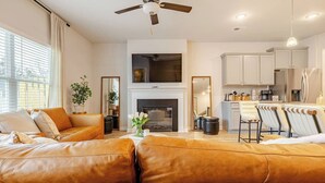 A modern living room with leather sofas, a fireplace, a kitchen area, and a dining set.
