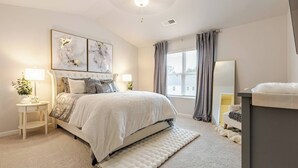 A bedroom with a large bed, a bedside table with a lamp, a mirror, and a window with curtains.