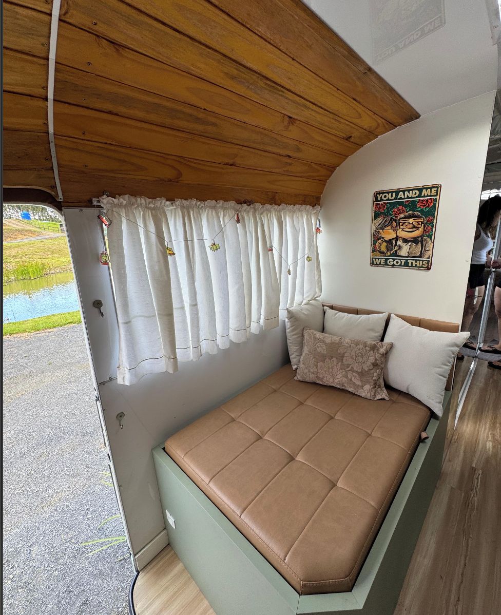 A compact, well-lit interior with a single bed, a wooden ceiling, and a view of the outdoors through a window.