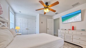 Een slaapkamer met een bed, een plafondventilator, een dressoir en een aan de muur bevestigde televisie.