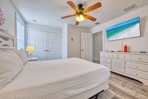 A bedroom with a bed, a ceiling fan, a dresser, and a wall-mounted TV.