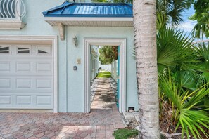 A pathway leading to a house with a garage, a light blue exterior, and a palm tree.