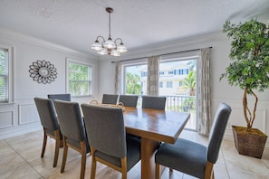 A dining area with a wooden table, grey upholstered chairs, a decorative wall clock, and a hanging light fixture. - 5 bed Home W/ Private Pool on Siesta Key! (Siesta Key)