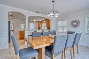 A dining area with a wooden table and six chairs, a kitchen in the background, and a decorative wall clock. - 5 bed Home W/ Private Pool on Siesta Key! (Siesta Key)