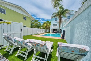 A backyard with a swimming pool, white lounge chairs, and a white fence.